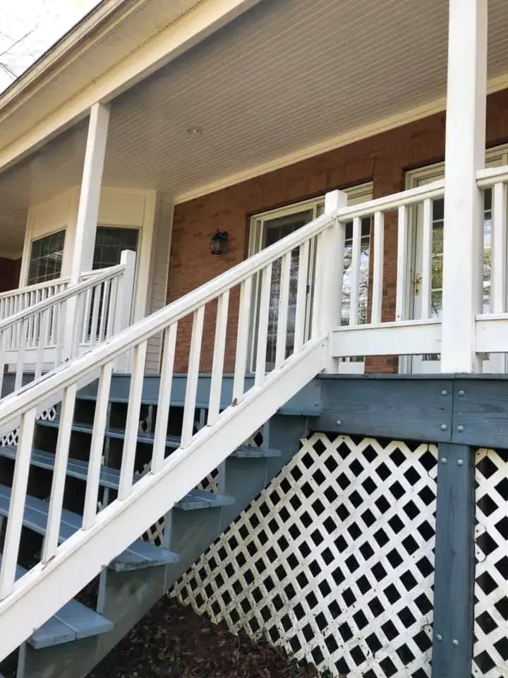 Wooden porch with stairs, white railings, and lattice skirting leading to a brick house. - My Personal Painter - My Personal Painter In progress: wraparound porch on brick Cape Cod: railings white, floor painted blue-gray