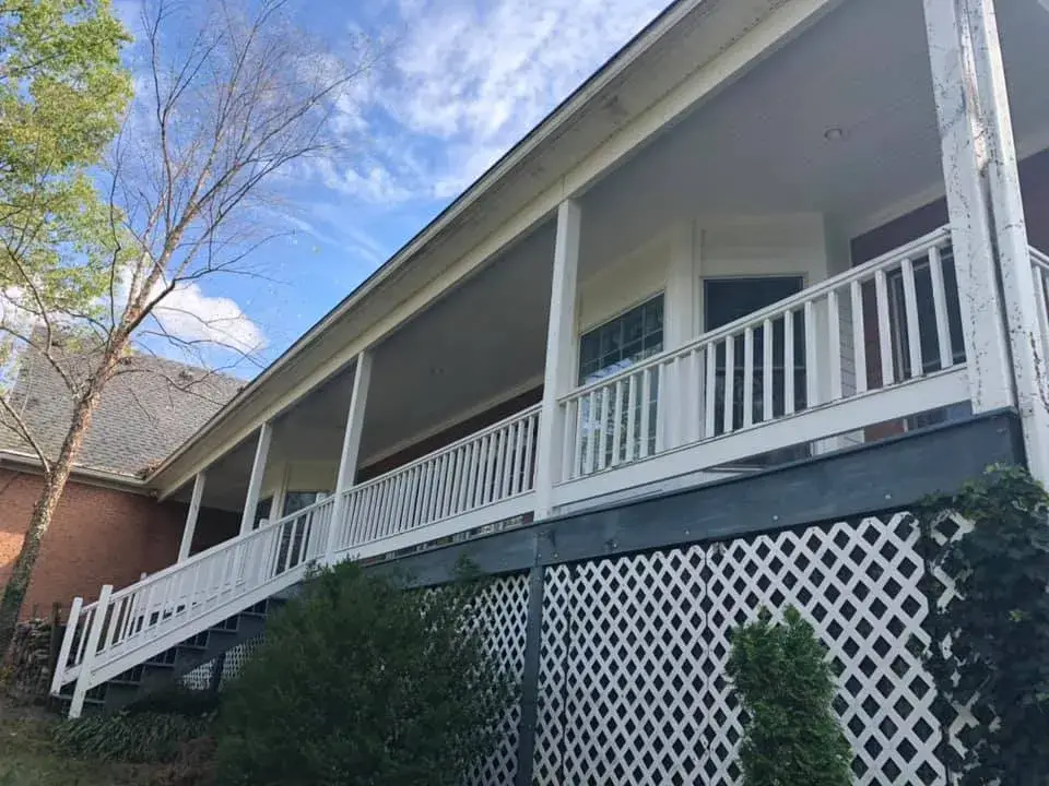 A house with a long, raised porch featuring a white railing and lattice skirting. - My Personal Painter - My Personal Painter In progress: wraparound porch on brick Cape Cod: railings white, floor painted blue-gray